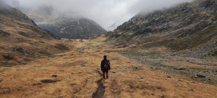 Una figura camina per una vall de muntanya sota la boira